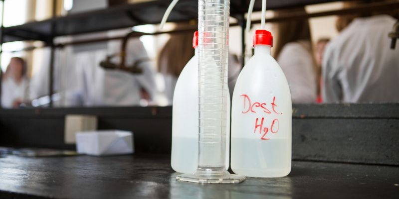 Distilled purified deionised water in plastic bottles with a pump. Measuring graduated cylinder for measuring water volume — Photo